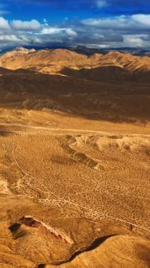 Bulutlar Kaliforniya çölündeki dağları ve tepeleri gölgeliyor. Karşıt mavi gökyüzü ve sarı karanın güzel yüksek açılı manzarası. Dikey video