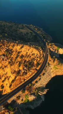 Hız otoyolu nadiren büyüyen ağaçlarla çevrili. Güzel sakin göl dağın eteğindedir. Üst Manzara. Dikey video