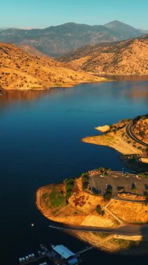 Eğri büğrü dağlarla çevrili gölün muhteşem güneşli manzarası. Drone otoparka ve kayadaki gözlem güvertesine yaklaşıyor. Dikey video