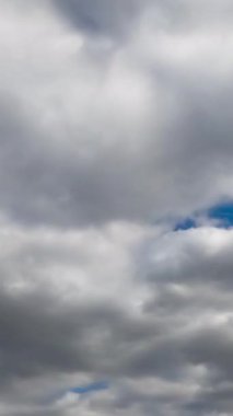 Mavi gökyüzünü tamamen kaplayan gri bulutlar. Düşük açı. Zaman ayarlı. Dikey video