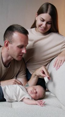 Mutlu ebeveynler yeni doğan çocuklarına bakıyor. Önemseyen baba, çocuğun sarı saçlarını fırçayla tarar. Dikey video