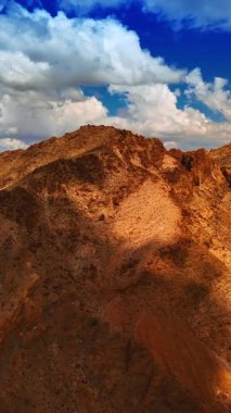 Kahverengi kayalar gök mavisi ile çelişiyor. Mojave çölündeki dağların üzerinde asılı beyaz bulutlar. Dikey video