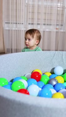 Renkli toplarla oynayan güzel bir bebek. Yumuşak havzada plastik topları olan şirin bir çocuk. Dikey video