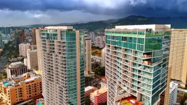 Waikiki 'deki yüksek katlı apartmanların arasında Ala Wai Kanalı' na doğru uçuş. Arkaplanda kara bulutlarla kaplı dağlarla Honolulu 'nun manzarası gözler önüne seriliyor..