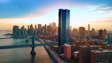 İnsansız hava aracı Doğu Nehri 'nin su yüzeyine iniyor. Güneşli New York manzaralı Manhattan Köprüsü ve Brooklyn Köprüsü manzaralı gün batımında.