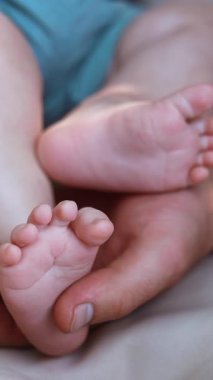 Babamın eli nazikçe küçük bir bebek ayağını tutuyor. Baba onlara dokunurken bebek ayaklarını savuruyor. Kapat.. dikey video