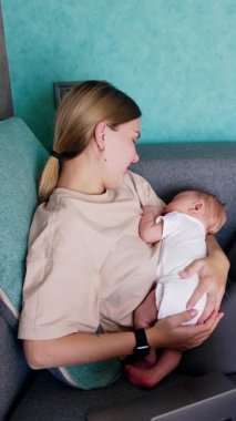Mutlu anne kanepeye yeni doğmuş bir bebekle rahatça oturur. Kadın bebeğin başını nazikçe okşar ve sonra dizüstü bilgisayara döner.
