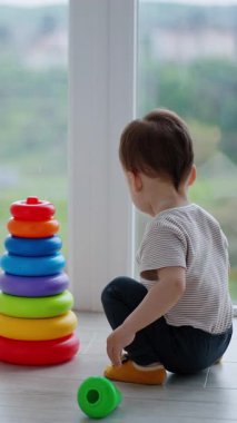 Bebek çocuk renkli oyuncak piramidini monte etti. Çocuk tepeye çıkmak istiyor ama dikkati başka bir şeye kayıyor ve geri çekiliyor.