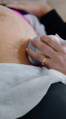 Hamile kadın ultrasonik teçhizatla muayene edilir. Sıhhiye cihazı bir hastanın karnında tutuyor. Kapat.. dikey video