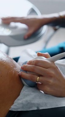 Hamile bir kadının ultrason muayenesi görüntüsü. Sıhhiyenin eli cihazı karnında tutuyor ve diğer el de ultrasonik makineyi çalıştırıyor. Kapat.. dikey video