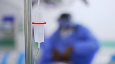 Tuz çözeltisi atık deposunun içine damlıyor. Ameliyathanede serum damlatılıyor. Kapatın. Arka planda mavi üniformalı bir sıhhiyenin bulanık görüntüsü.
