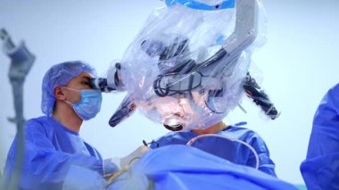 İşbirliği yapan iki cerrah mikroskop ameliyatına bakıyor. Odaklanmış doktorlar sinir cerrahisi yaparlar. Düşük açı görünümü.