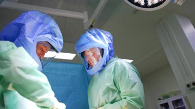 Koruyucu kasklı beyaz cerrahlar operasyonda çalışıyor. Travma cerrahlarının görüş açısı düşük..