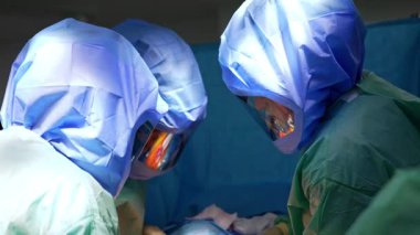 Koruyucu miğferli üç doktor hastaya yaslanıyor. Doktorlardan biri iplik kullanıyor..