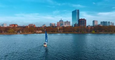 Mavi yelkenli tekne parkla birlikte rıhtıma gidiyor. Arka planda Boston 'un silüeti. Hava perspektifi.