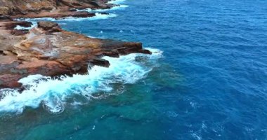 Güzel köpüklü dalgalar kayalara çarpıyor. İnsansız hava aracı görüntüleri Pasifik Okyanusu 'nun göz kamaştırıcı mavi su manzarası üzerinde..