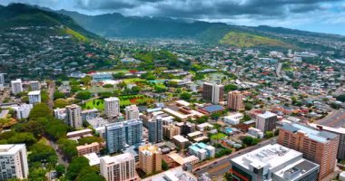 Bir sürü yeşillikle pitoresk şehrin üzerinde uçmak. Arkaplandaki yoğun bulutların altındaki yemyeşil dağlar. Honolulu, Hawaii, ABD.