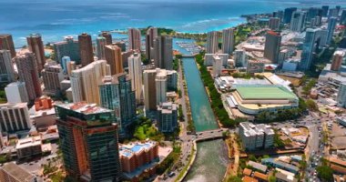 Arabalar Waikiki 'yi ayıran Ala Wai Kanalı üzerindeki köprüden geçiyor. Şehrin yüksek katlı modern mimarisi üzerine gökyüzü perspektifi mavi su manzarasının arka planında.