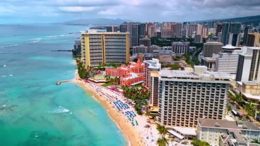 Waikiki 'nin lüks kumlu plajında ilerliyoruz. Turkuaz su kıyıya vuruyor. İHA görüntüleri şehir manzarasının üstünde.