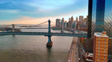 Manhattan ve Brooklyn Köprüleri, Doğu Nehri üzerinde. Batan güneş Manhattan, New York, ABD 'nin gökdelenlerini kamaştırıyor.