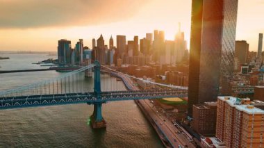 Manhattan Köprüsü yakınındaki yüksek katlı cam kuleden uzakta. Güneşin batışı gökdelenlerin arkasından manzarayı kamaştırıyor. New York, ABD.