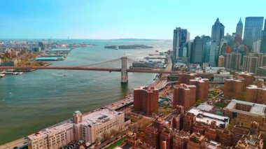Manhattan rıhtımının üzerinden Brooklyn Köprüsü 'ne yaklaşıyoruz. Günbatımında Doğu Nehri ve New York şehir manzarasına hava perspektifi.