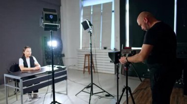 Genç bayan masada oturuyor. Kameraman ekipmanları bayanın etrafına yerleştirir. Stüdyo çekimi.