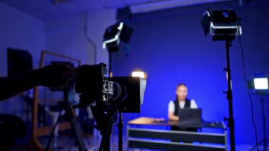 Tanınmayan bir kameramanın eli tripoddaki çalışan bir kameraya dokunuyor. Kadın blogcu bulanık arkaplanda bir video günlüğü kaydediyor.