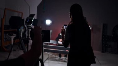 Blog ekibi stüdyoda çalışıyor. Kadın blogcu masada oturuyor. Erkek ve kadın akıllı telefon ve profesyonel kamerayla video çekiyor..