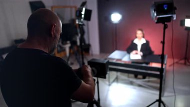 Siyah tişörtlü yetişkin adam kameraya bakıyor. Kameraman kadın blogcuyla bir video kaydediyor.