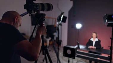 Stüdyoya kamera yerleştiren profesyonel bir kameraman. Kadın blogcu, blog görüntülerine hazırlanmak için masada oturuyor.