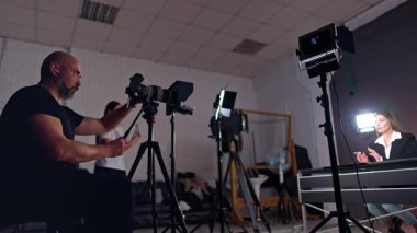 Konsantre beyaz kameraman kameranın objektifine bakıyor. Esmer kadın blog için kamera kayıt videosuyla konuşuyor.