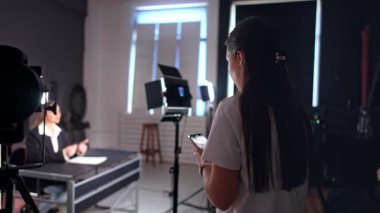 Beyaz tişörtlü uzun saçlı esmer, masada oturan bir kadının videosunu çekmeye başlıyor. Blogcular blog için içerik oluşturur.
