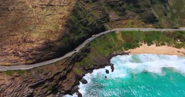 Arabalar dağ yamacındaki tehlikeli yoldan ilerliyorlar. Okyanusun köpüklü dalgaları kayalık kıyıya ulaşır. Hava görünümü.
