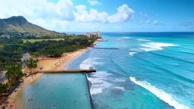 Hawaii 'deki muhteşem kumlu plaj. Büyüleyici dalgalar kıyıya vuruyor. Rıhtımdaki yemyeşil alan ve arka plandaki Diamond Head Krateri. Hava görünümü.