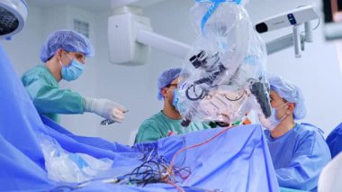 Erkek asistan hazır bir cerrahi metal alet tutuyor. İki cerrah mikroskoba bakar ve nörocerrahi yapar..