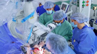 Beyin cerrahlarından oluşan profesyonel bir ekip beyin ameliyatı yapıyor. Erkek cerrahlar mikroskop ameliyatına bakarlar. Üst görünüm.