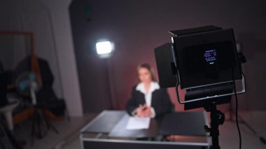 Işıklandırma ekipmanları stüdyoda. Siyah ceketli ve beyaz gömlekli kadın bulanık arka planda oturuyor..