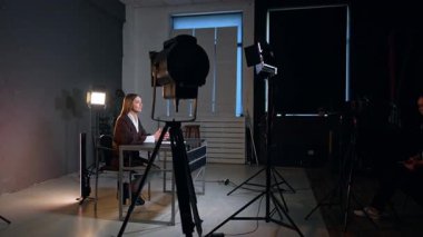 Video çekmek için ekipmanlı modern fotoğraf stüdyosu. Kadın blogcu blogu için video çekiyor. Sahne arkasında oturan beyaz kız telefonunu görüntü için kullanıyor..