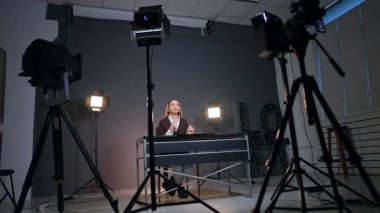 Beyaz kadın bir video kaydederken masasında oturmuş konuşuyor ve el kol hareketi yapıyor. Blog içeriğinin stüdyo görüntüleri. Düşük açı görünümü.