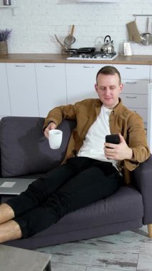 Evde cep telefonu kullanan bir adam. Evdeki kanepede dinlenen ve cep telefonu kullanan genç bir adam. Dikey video