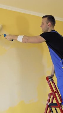 Paten fırçalı boya duvarı. Duvarı boyayan genç adam, paten fırçası kullanıyor. Dikey video