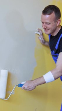 Yeni dairede tamirat yapan bir adam. Genç adam dairesini yenilerken duvarları fırçayla boyuyor. Dikey video