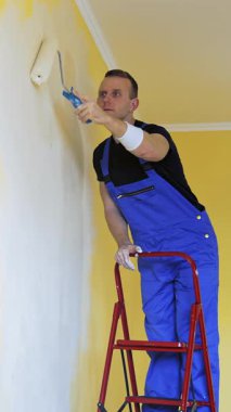 Adam dairenin duvarlarını boyuyor. Kafkasyalı adam duvarı silindirle boyuyor. Dikey video