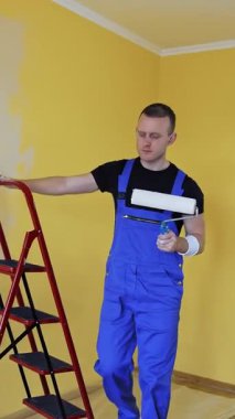 Tekerlekli adam boyası. Üniformalı işçiler duvarları boya rulosuyla boyuyor. Dikey video