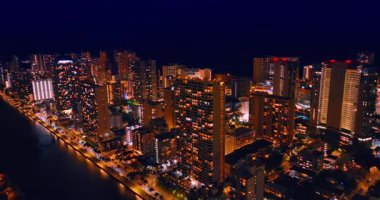 Waikiki tatil köyü civarındaki binalar ve sokaklar geceleri iyi aydınlatılır. Koyu mavi arka planda parlak bir şehir. Hava görünümü.