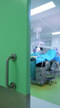 Ameliyat odasına açılan sürgülü kapı. Tanınmayan doktor ameliyat masasında çalışıyor. Dikey görünüm.