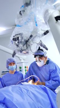Cerrahi loupes cerrahı ameliyat aletini uygular. Ameliyat hemşiresi yanında duruyor. Mikroskop doktorun üstünde. Dikey video.