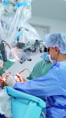 Kafkas cerrahı elektrikli alet kullanır ve hemşireye verir. Doktor mikroskop altında ameliyat yapar. Dikey video.