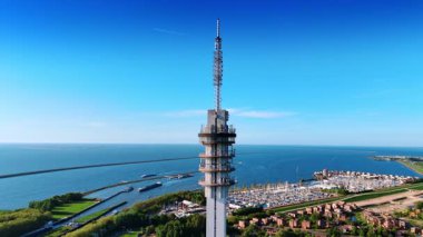 Telekom kulesinin tepesinde, mavi gökyüzü ve Hollanda 'daki Houtrib Harbor, Lelystad' ın masmavi su manzarası. Arka planda rıhtımda birden fazla yat var. Hava perspektifi.